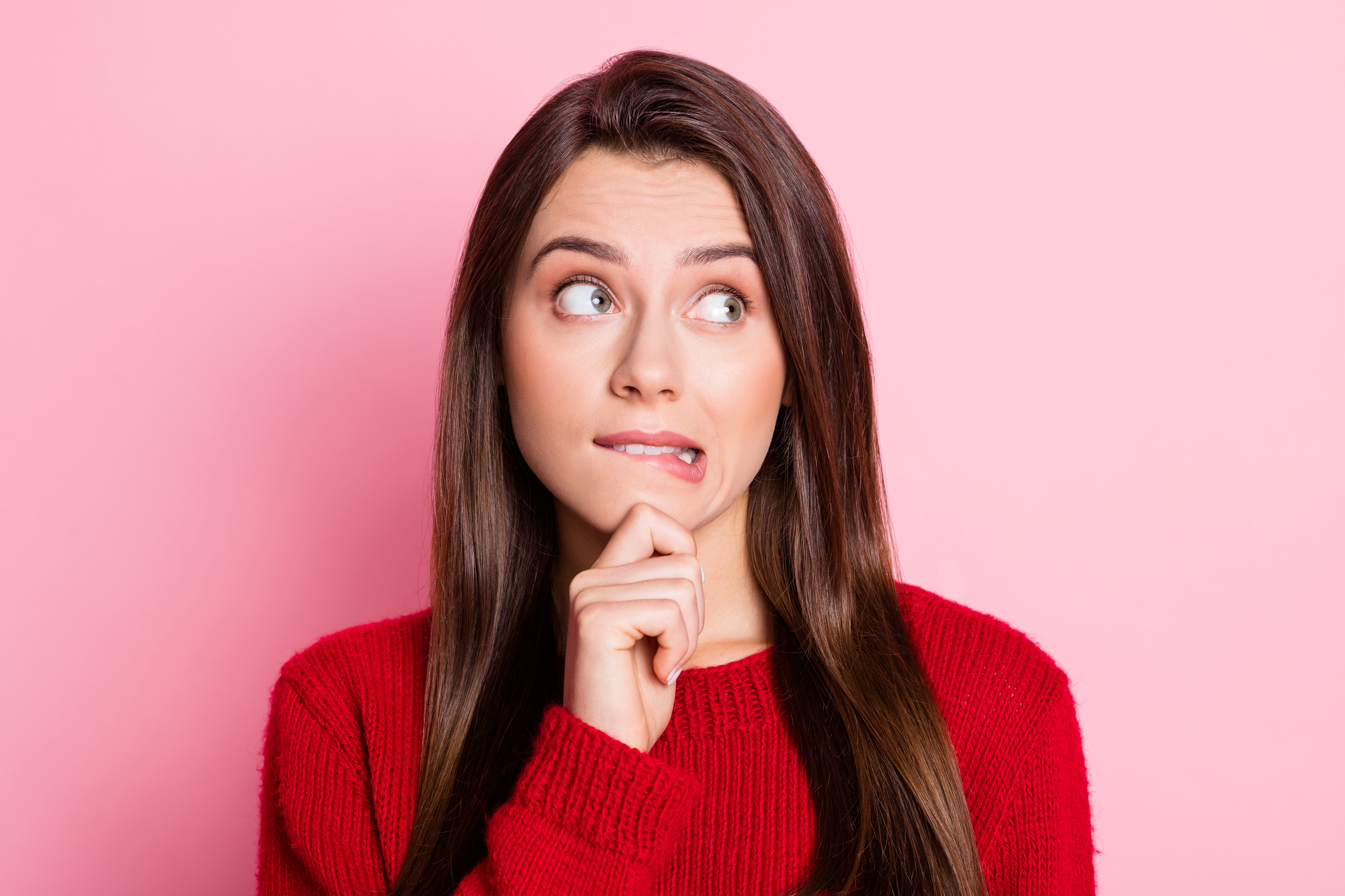 A young woman in a red sweater looking uncertain and biting her lip, representing confusion or hesitation, often experienced during an elevator pitch at career fairs.