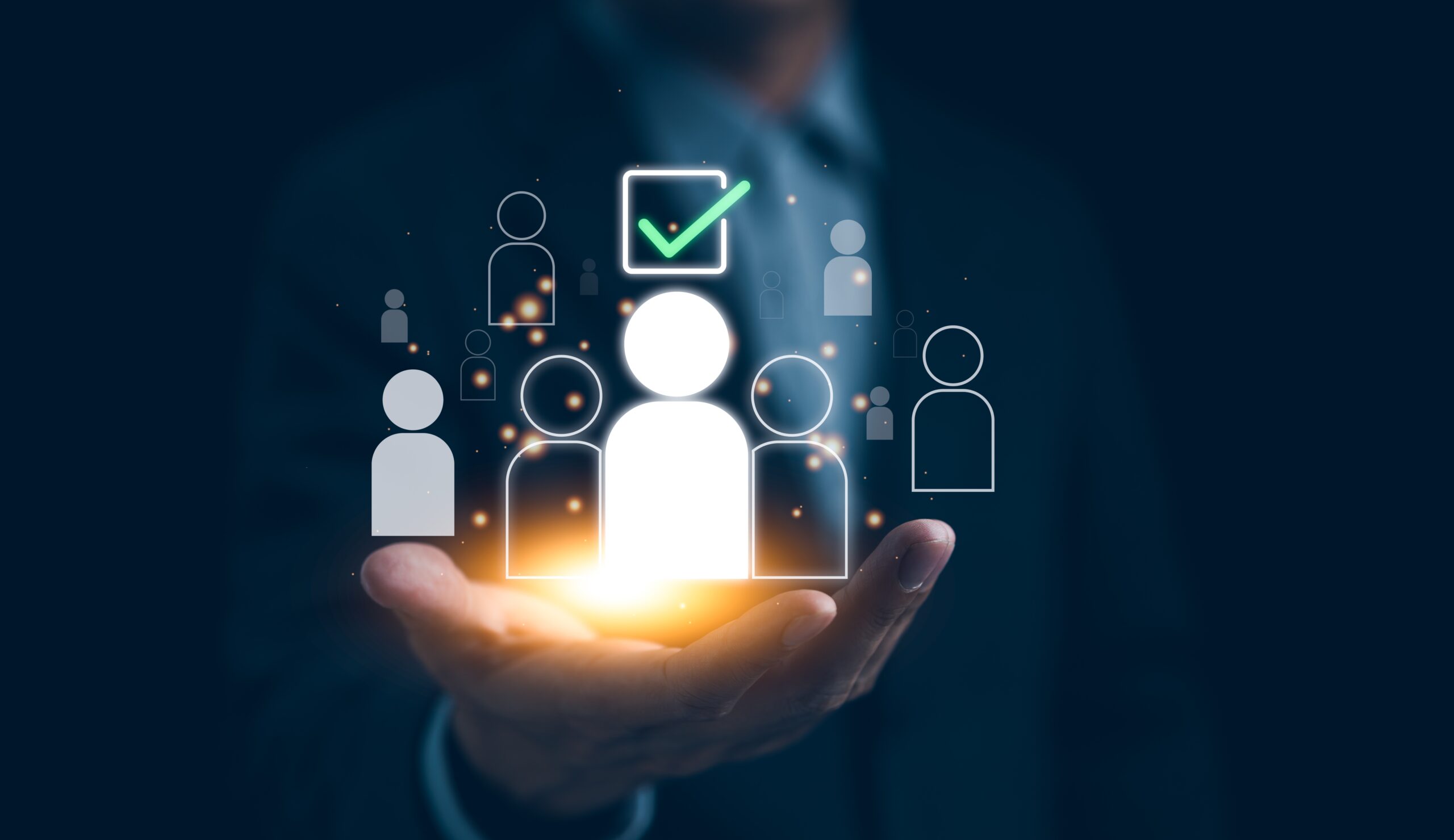 A businessman holding digital icons of people in his hand, with a glowing selected figure and a green checkmark symbol, representing recruitment, hiring, or talent selection.