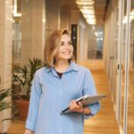 A confident woman walking through a modern office hallway holding a laptop, symbolizing career growth and opportunity.