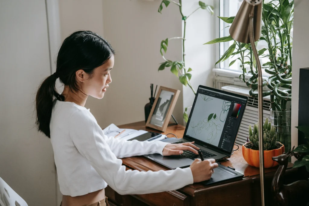 What Jobs Hire At 14 And 15 – teen working on graphic design using a laptop and drawing tablet, representing creative online job opportunities for teenagers.